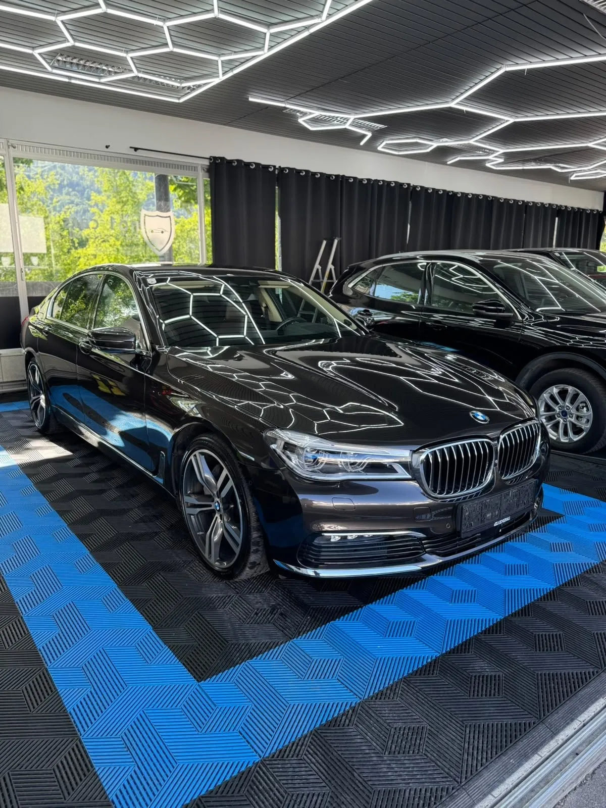 BMW 7er in der Halle von Saff Car Lounge in Kufstein nach der Aufbereitung, Hexagon-Leuchten spiegeln sich im Lack