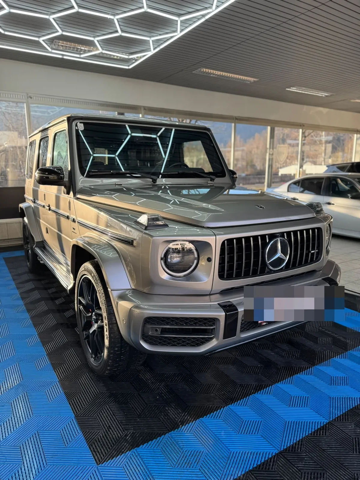 Blick in die Halle: Hexagon-LED-Leuchten an der Decke, blaue Bodenfliesen, Mercedes G-Klasse